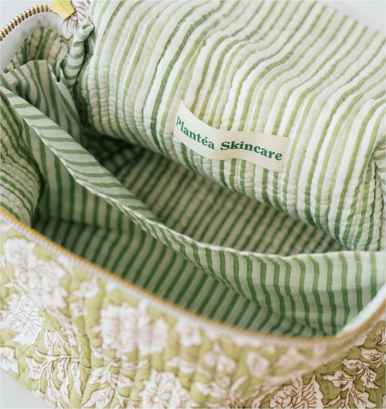 Open green and white floral toiletry bag with striped interior labeled "Plantea Skincare."