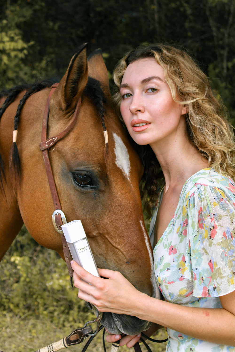 Woman holding a bottle next to a brown horse outdoors.